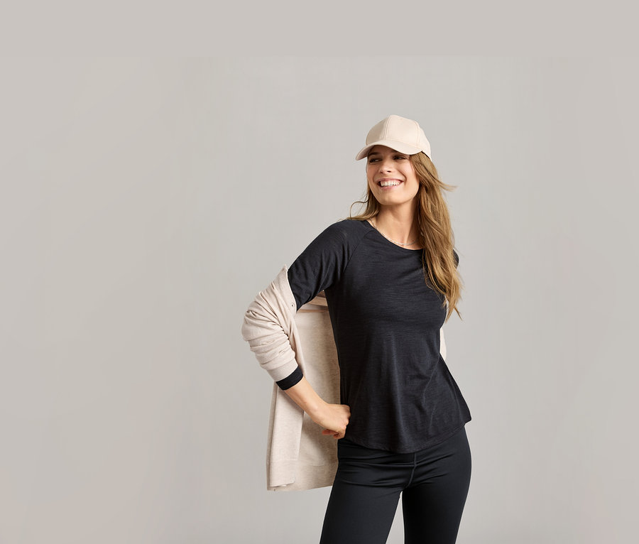 Femme portant une casquette beige et une chemise fonctionnelle noire. Elle porte un cardigan beige et un legging noir.