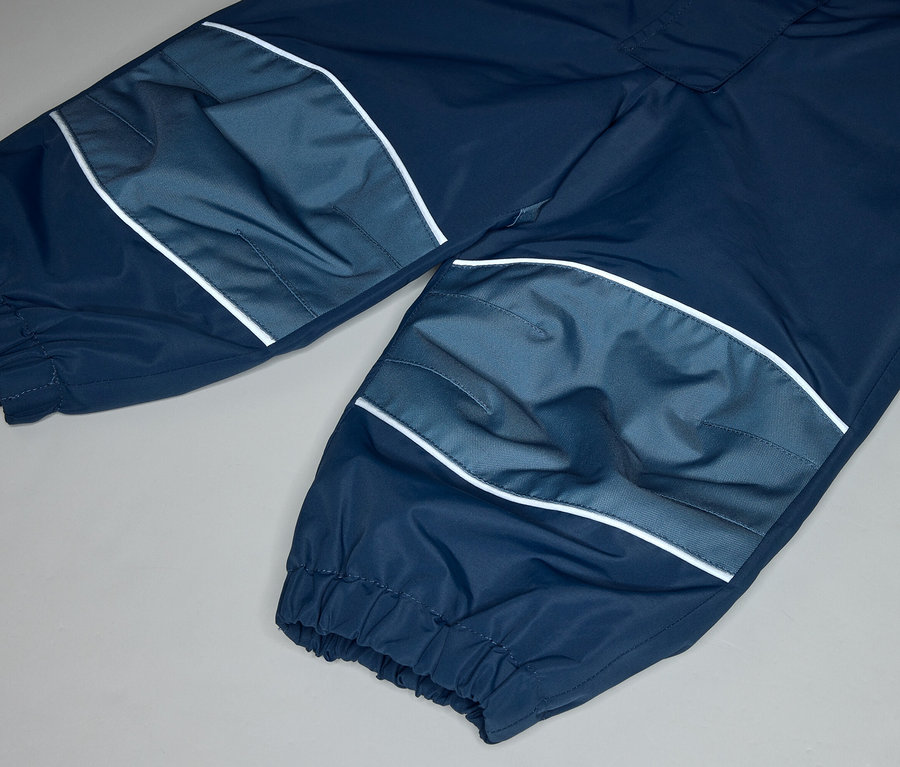 Gros plan d'un pantalon bleu marine avec des patchs genoux bleu clair et des rayures blanches sur fond gris.