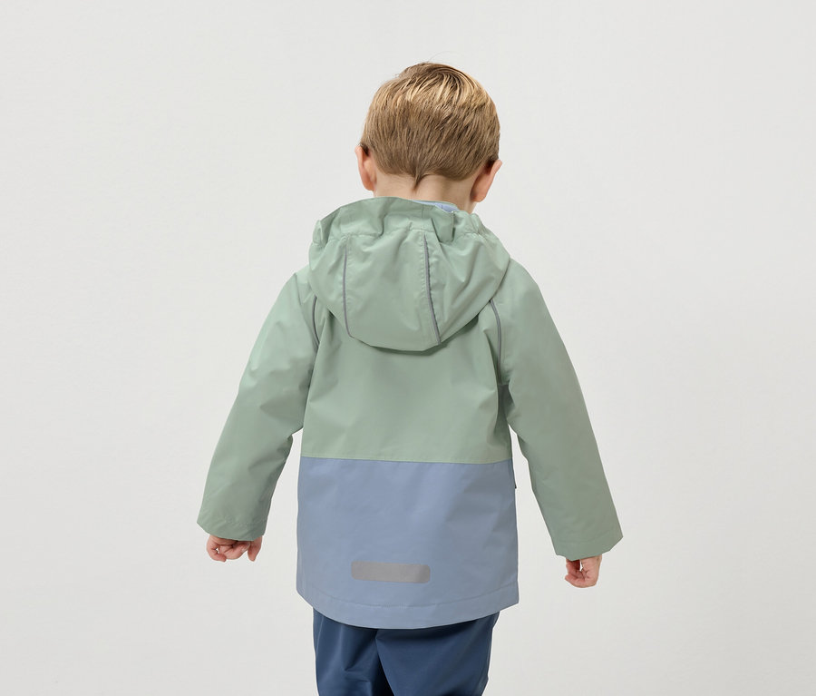 Vue arrière d'un enfant blond portant une veste bicolore verte et bleue.