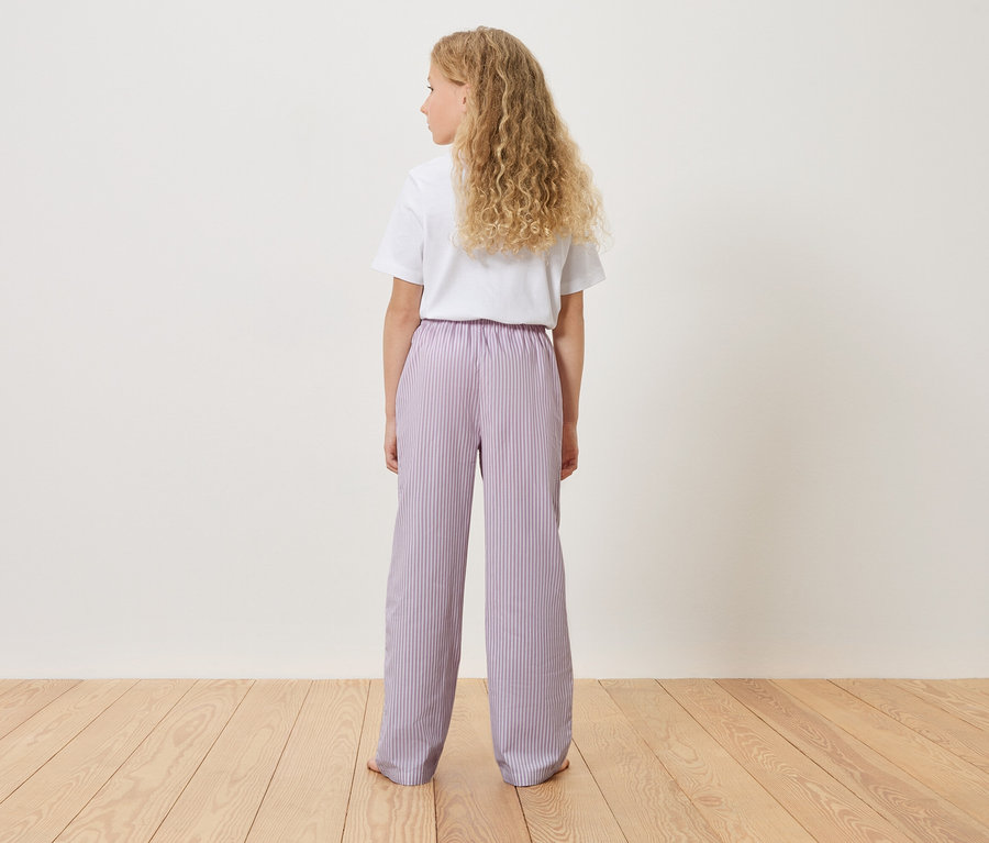 Vue de dos d'une jeune fille aux cheveux blonds et bouclés portant un t-shirt blanc et un pantalon rayé lilas clair.