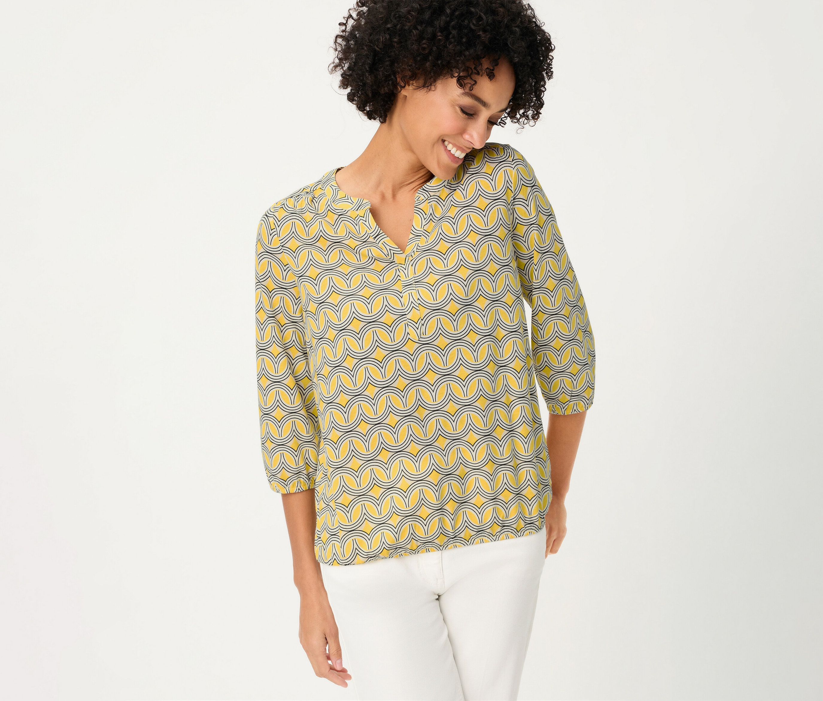 Une femme porte un chemisier Olsen 3/4 à motifs jaunes et un pantalon blanc.