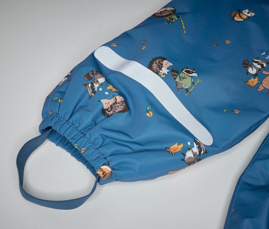 Gros plan d'une combinaison bleue avec des motifs d'ours, de ratons laveurs et de hérissons, une bande blanche et une bride élastique à la cheville.
