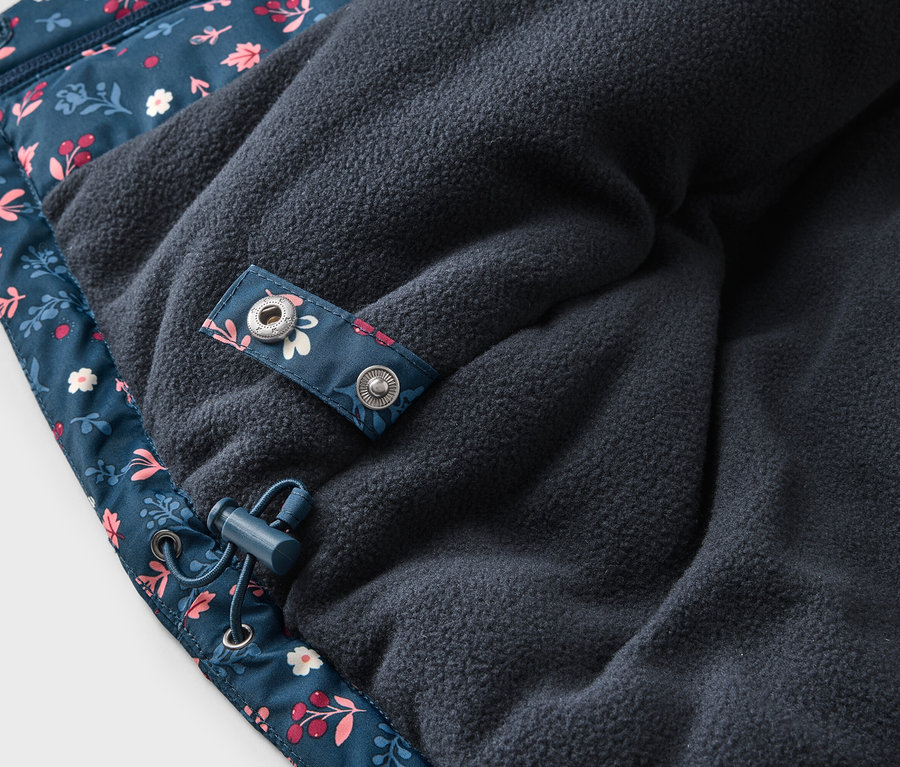 Gros plan sur une veste bleu marine à motif floral avec doublure polaire, cordon de serrage et bouton-pression.