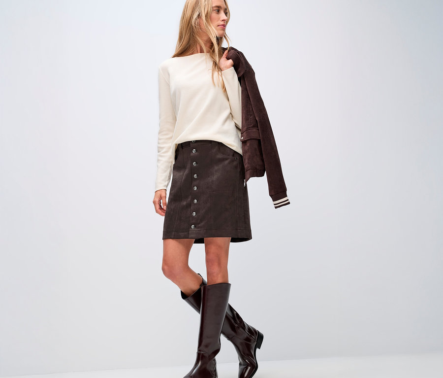 Femme portant un pull crème et une jupe de velours marron Street One boutonnée, des bottes marron et une veste marron sur l'épaule.