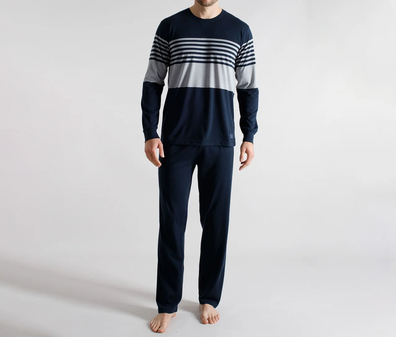 Homme debout pieds nus, portant un pyjama bleu marine à manches longues, avec un haut rayé gris et blanc sur la poitrine.
