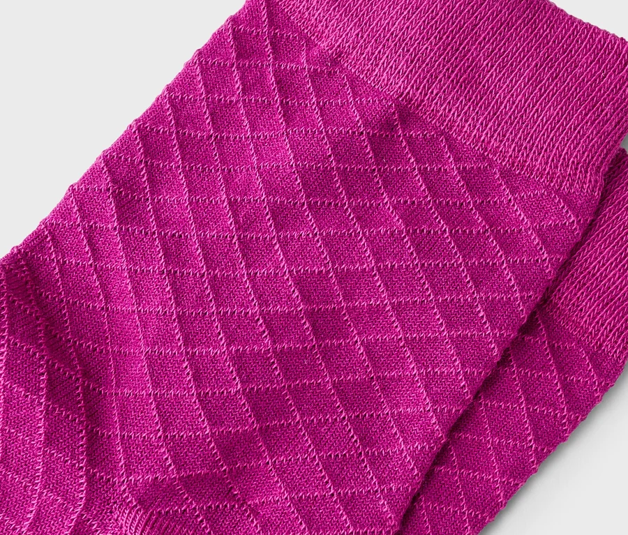 Deux chaussettes rose fuchsia avec un motif tricoté en losanges et des bords-côtes, légèrement superposées sur un fond gris clair.
