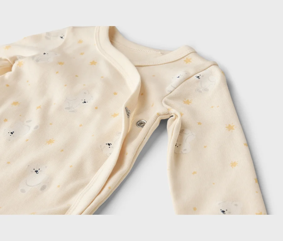 Gros plan d'un body bébé crème avec un motif d'oursons blancs et d'étoiles jaunes, doté de boutons-pression.