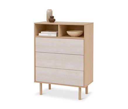 Commode en bois clair avec trois tiroirs beige clair, deux compartiments ouverts avec livres et un bol, et deux vases décoratifs sur le dessus.