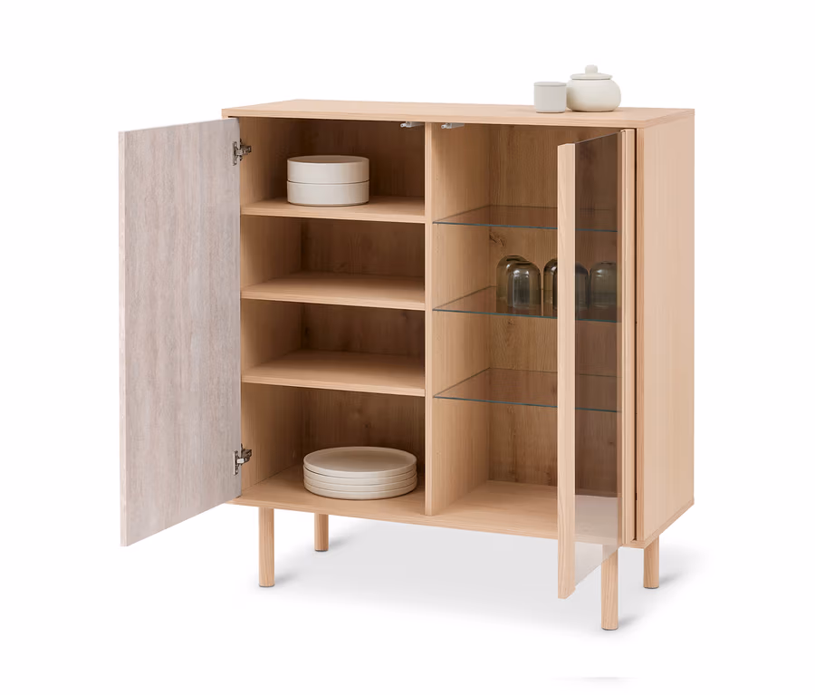 Meuble en bois clair avec deux portes ouvertes, une en bois et une en verre. À l'intérieur se trouvent des assiettes et des verres, et sur le dessus une tasse et un pot.