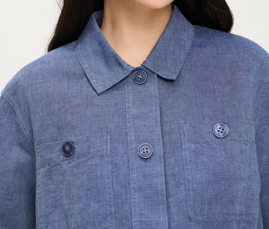 Gros plan d'une personne portant une veste en jean Olsen bleue avec un col, des boutons et des poches poitrine.