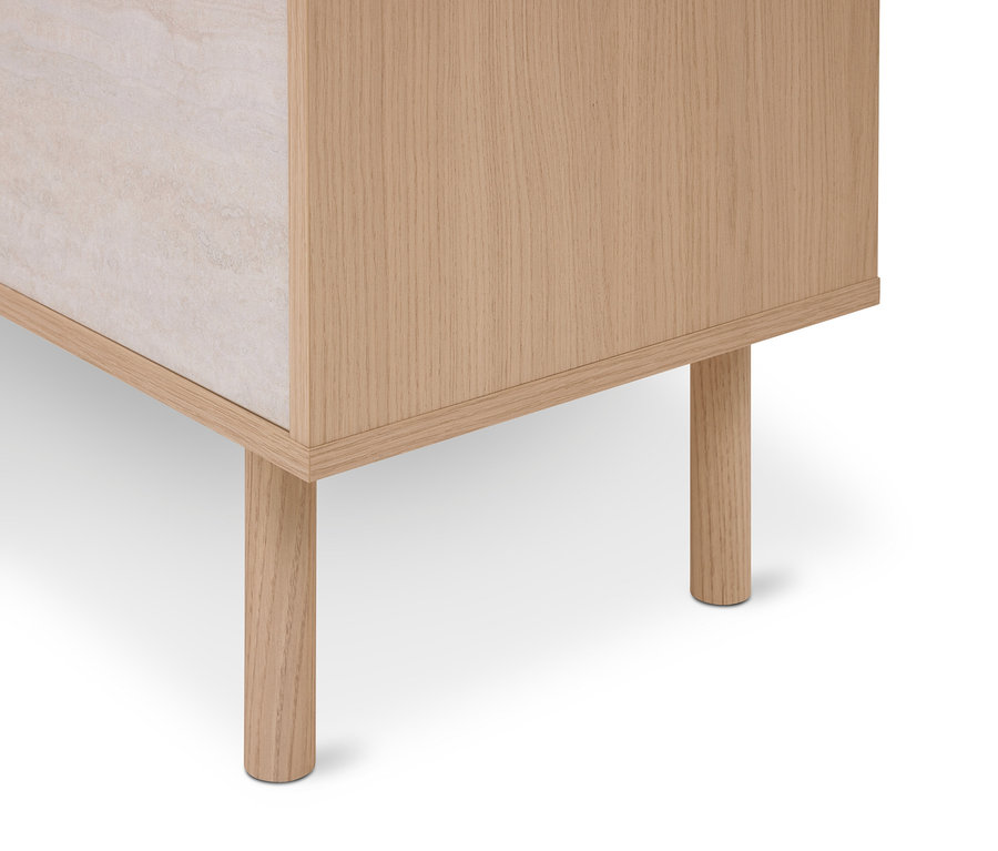 Coin inférieur d'une armoire en bois clair avec deux pieds cylindriques et un panneau en pierre beige clair.