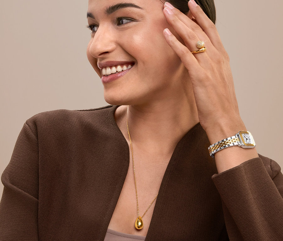 Femme souriante touchant son visage portant une bague, une montre et un collier en or.