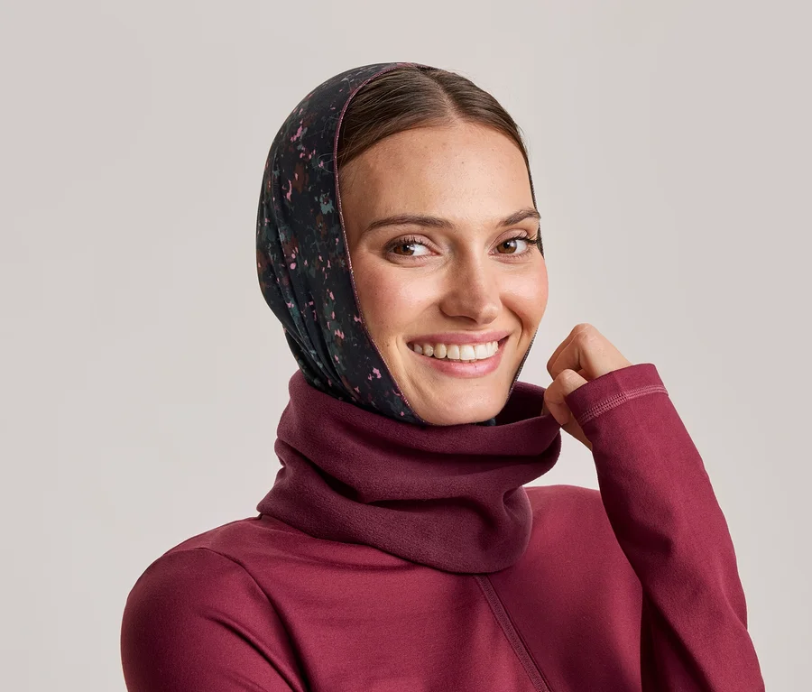 Femme souriante portant un foulard foncé à motifs floraux et un pull bordeaux à col montant, tenant le col.
