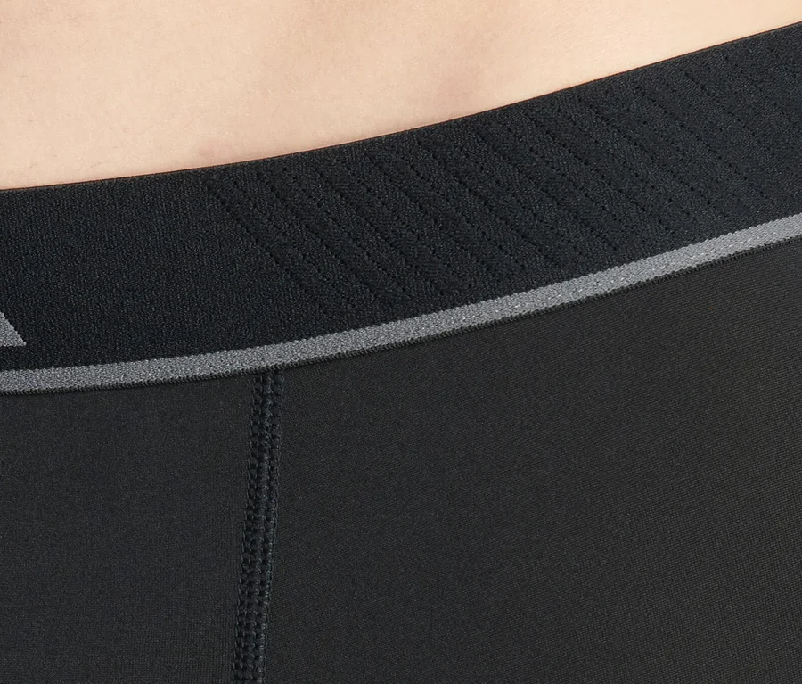 Gros plan sur la taille d'une personne portant un short de sport noir avec une ceinture élastique texturée, une bande grise et une couture visible.