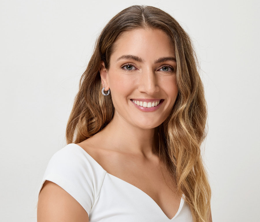 Une femme souriante aux longs cheveux bruns ondulés et portant des boucles d'oreilles.