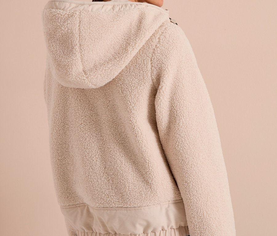 Femme de dos, légèrement tournée, portant une veste CECIL à capuche en polaire beige clair et un jean.