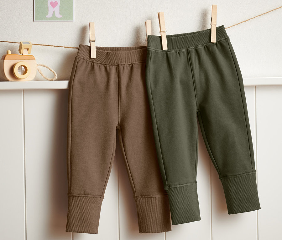 Deux pantalons de survêtement (2 pièces) marron et vert olive suspendus à une corde à linge.