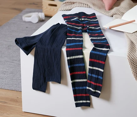 Deux leggings en maille reposent sur une surface blanche. L'un est bleu marine uni, l'autre a des rayures horizontales rouges, blanches et bleues.