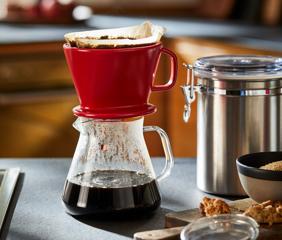 Une cafetière en verre avec un filtre à café rouge.