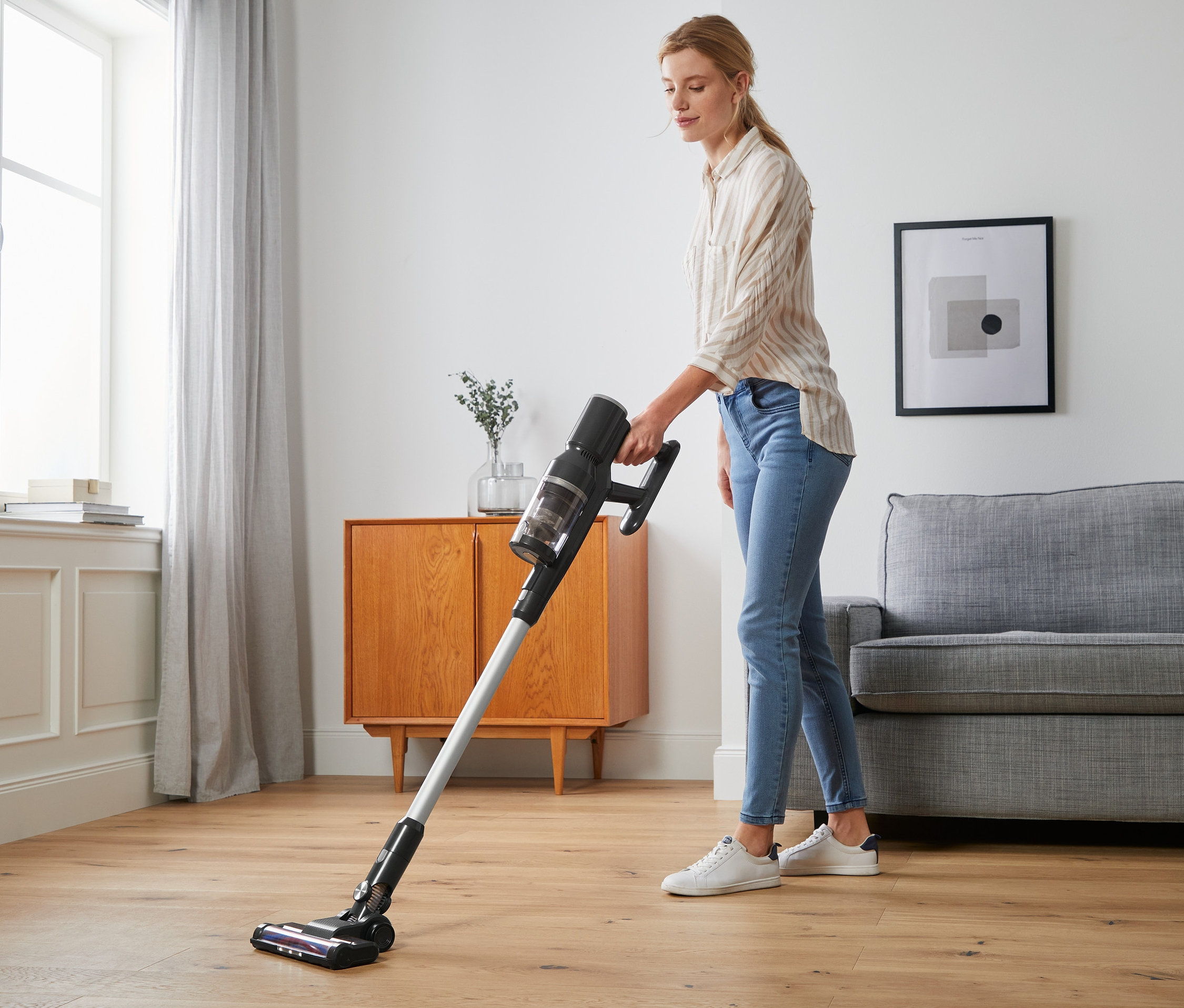 Une femme passe l'aspirateur sur le plancher avec un aspirateur numérique sans fil.