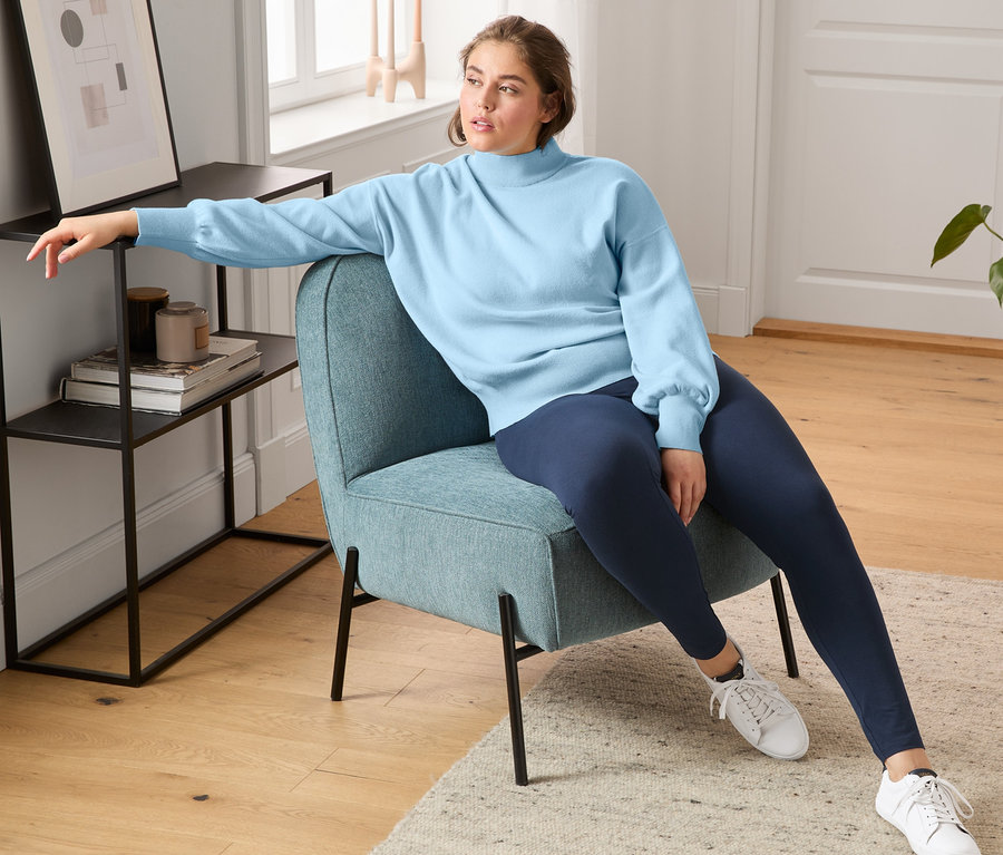 Une femme est assise dans un fauteuil et porte des baskets en cuir tanné sans chrome, un legging et un pull à manches ballon.