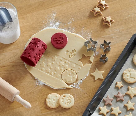 La pâte est abaissée avec un outil à biscuits 3-en-1 à motif étoilé. Des étoiles découpées et des biscuits finis sont à côté.