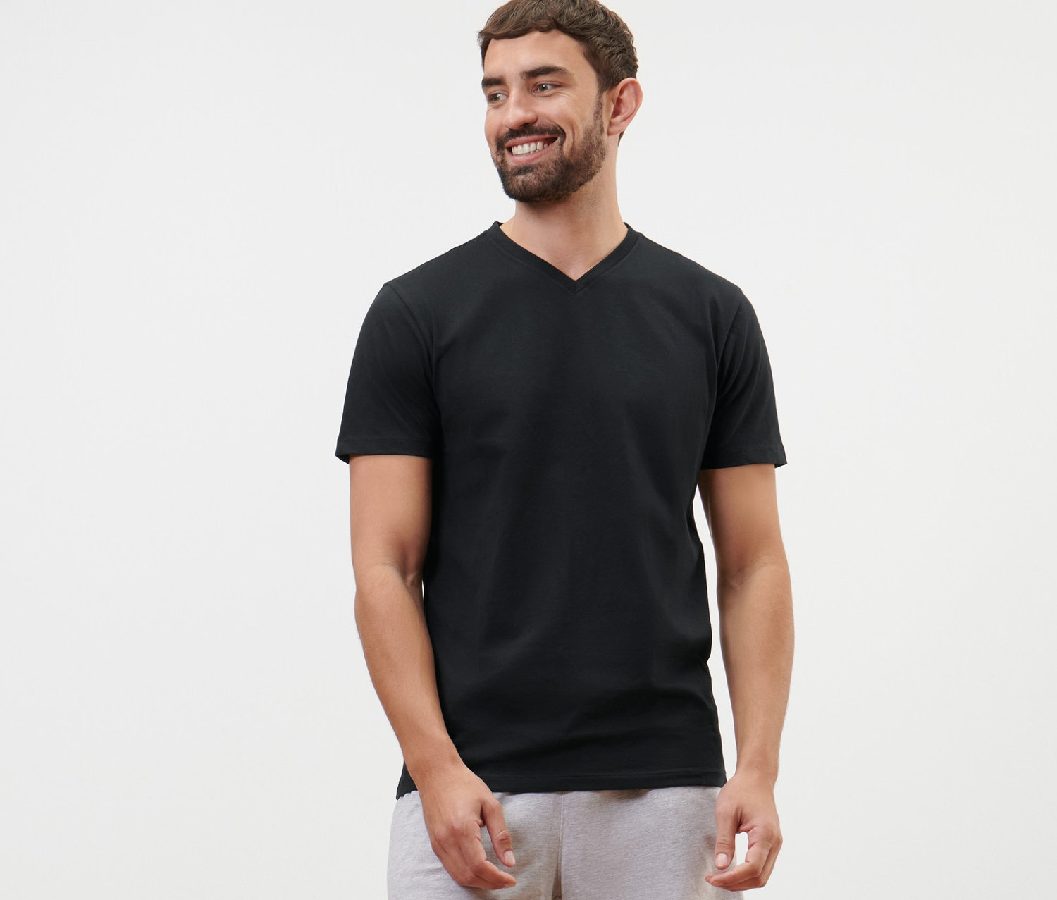 Un homme porte un t-shirt noir à col en V et un short gris.