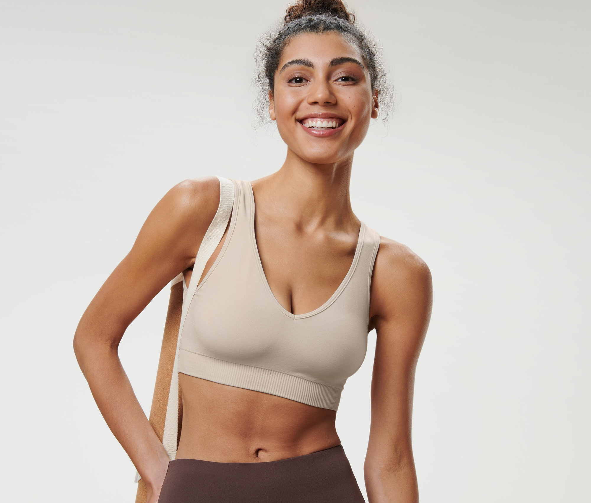 Une femme souriante portant une brassière de sport sans coutures, blanc cassé.