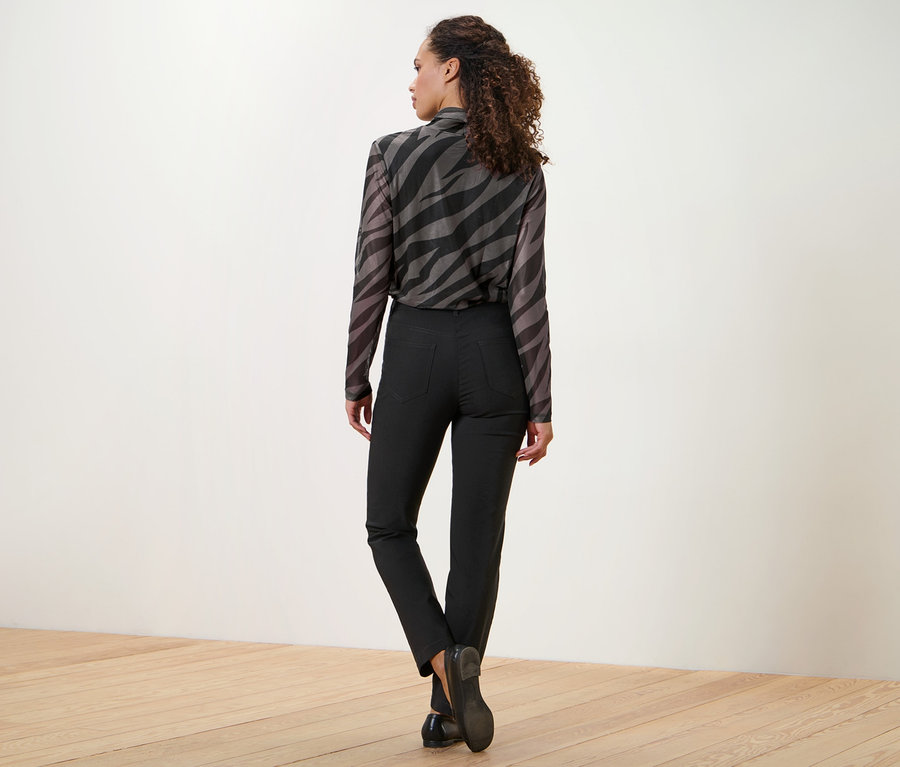 Une femme regarde par-dessus son épaule, portant un chemisier à imprimé animalier et un pantalon en bengaline noir.