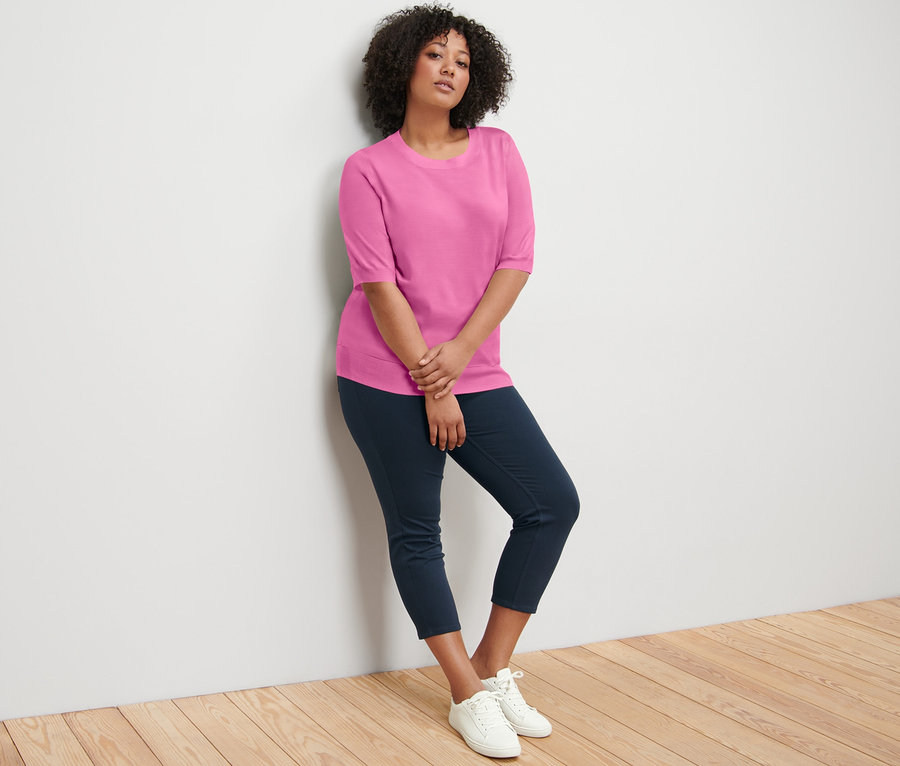 Femme appuyée contre un mur portant un jeggings 7/8 et un pull en maille fine.