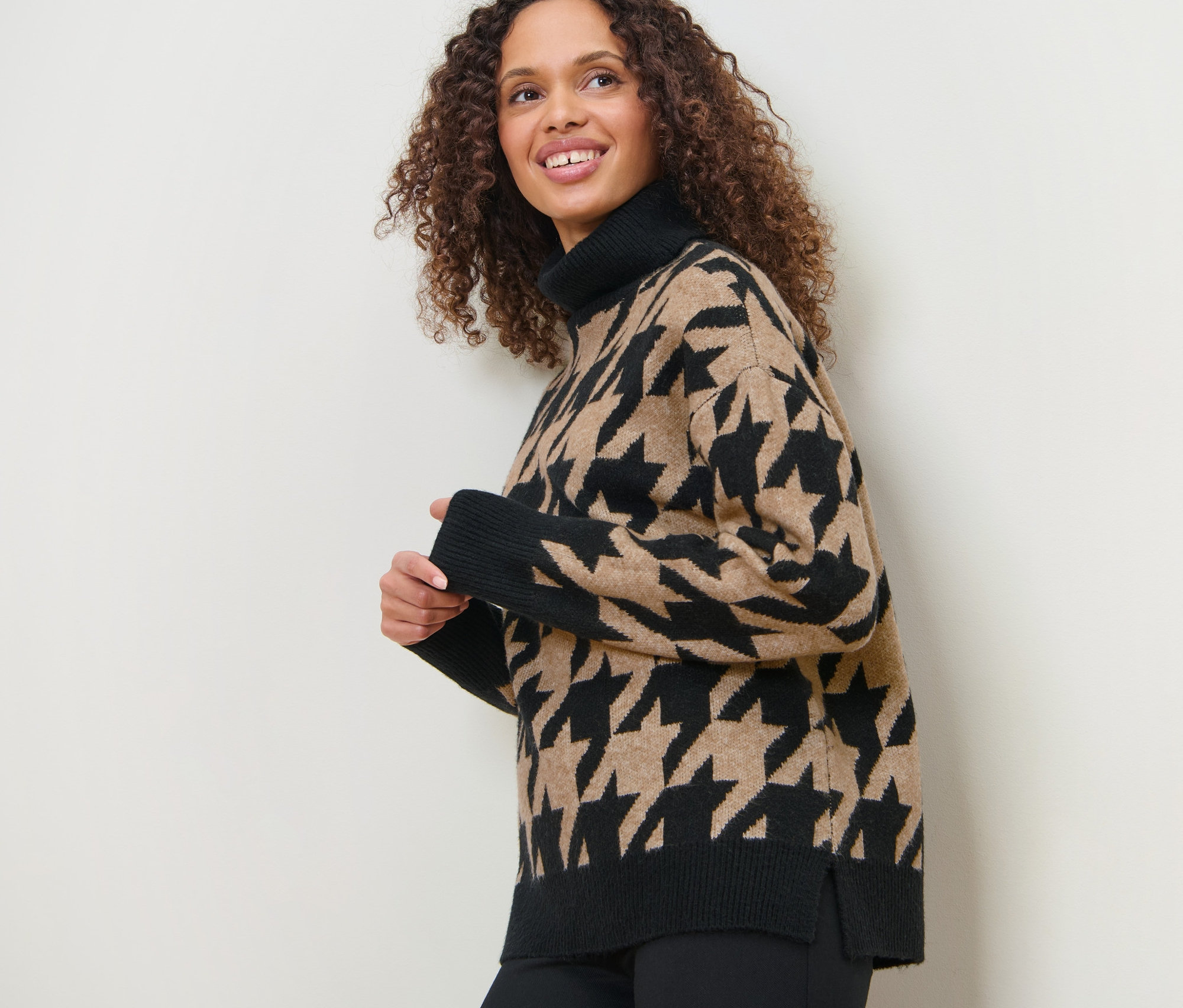 Une femme souriante pose, portant un pull en maille à jacquard pied-de-poule.