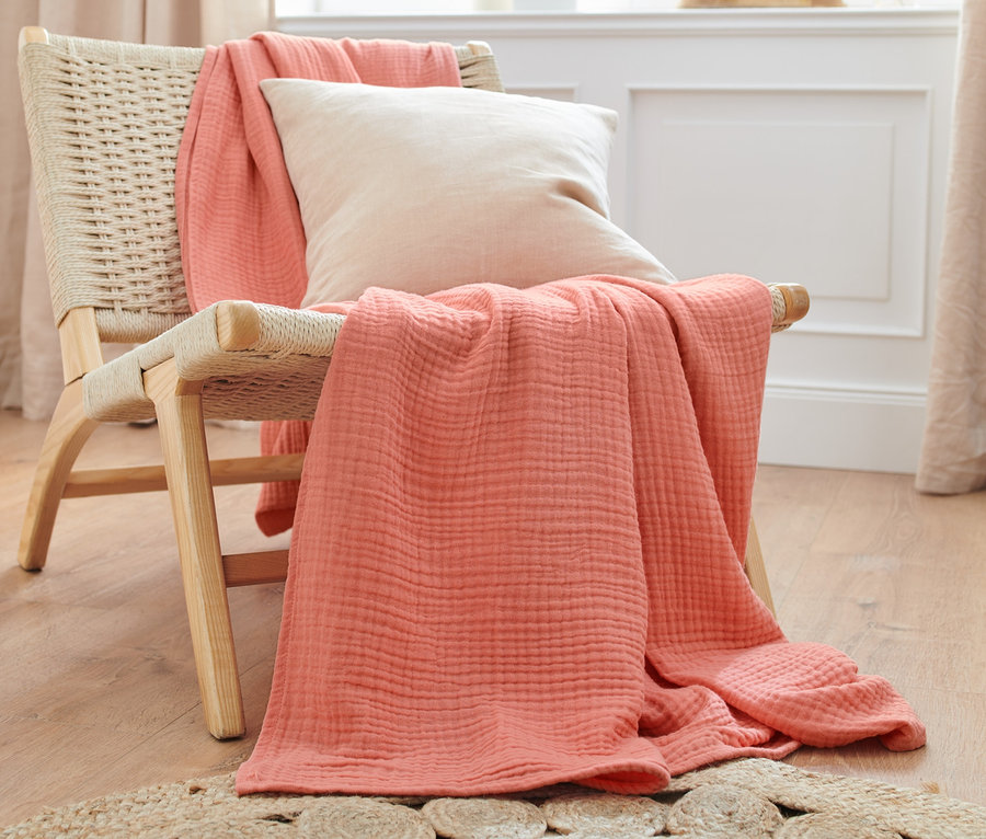 Un couvre-lit pêche et un coussin crème sont posés sur un fauteuil en osier.