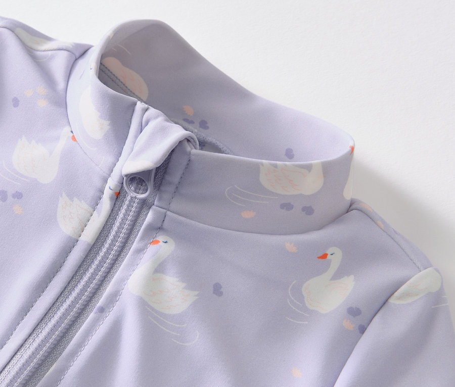 Gros plan sur une combinaison violette pour bébé avec fermeture éclair et motif de cygnes, indice de protection UV 80.