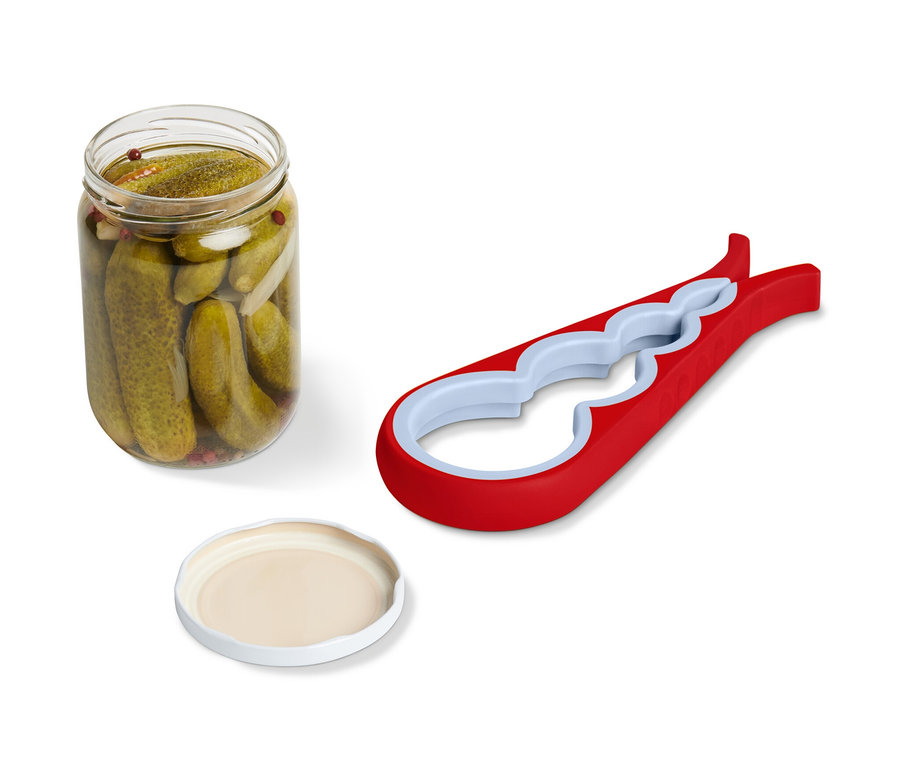 Un bocal de cornichons, un couvercle et un ouvre-bocal et ouvre-bouteille sont placés l'un à côté de l'autre.