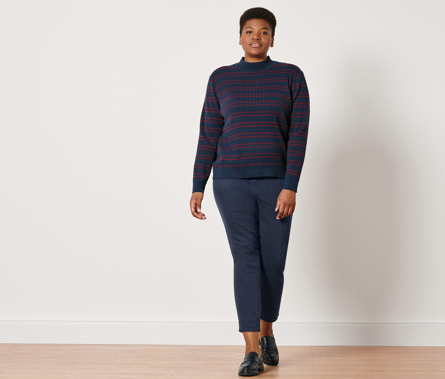 Femme posant en pantalon twill bleu foncé avec ceinture confort et pull en maille fine bleu rouge avec torsades.
