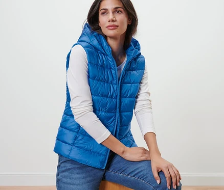 Une femme est assise et porte un gilet matelassé à capuche bleu.