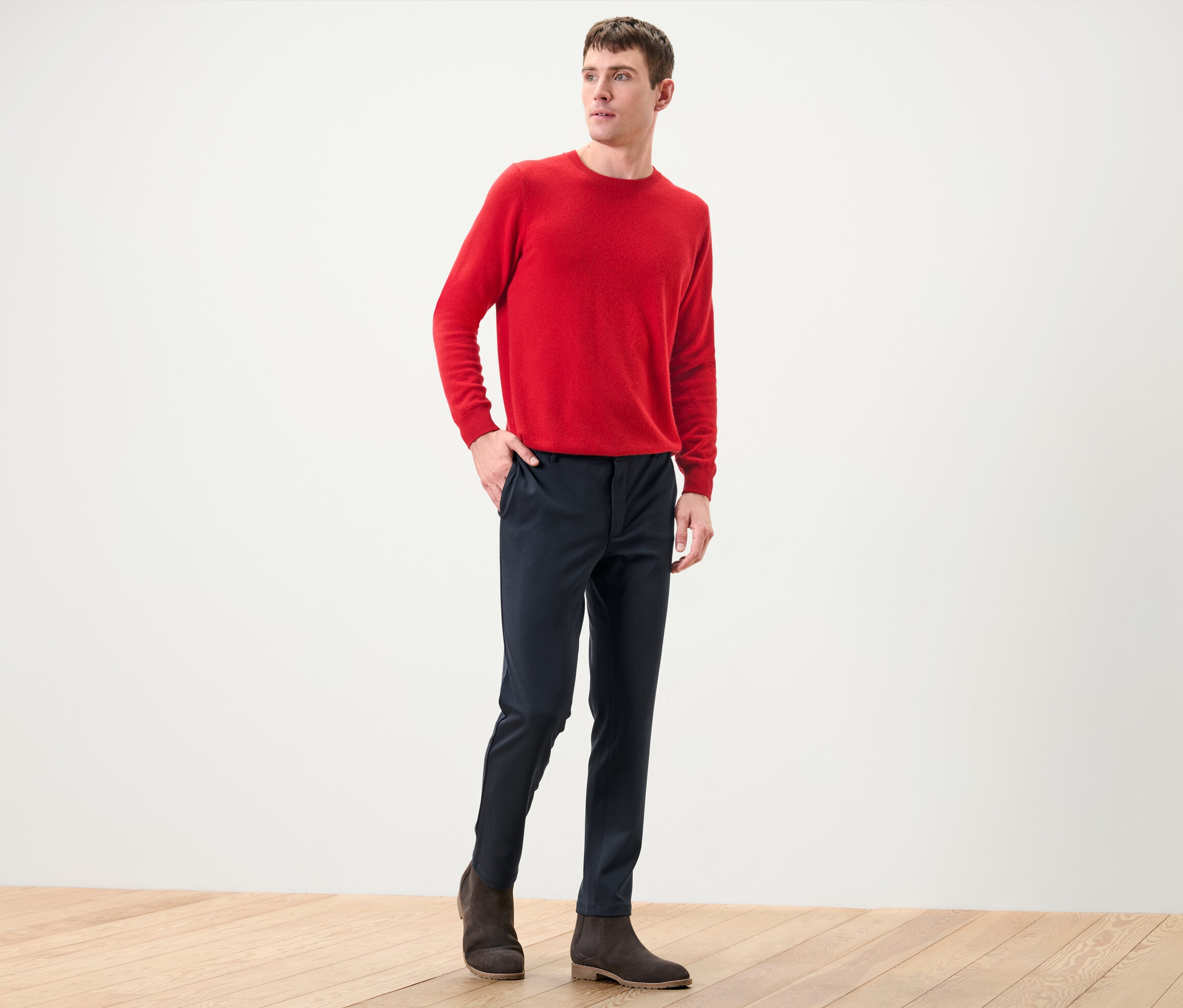 Un homme pose, portant un pull rouge et un pantalon confortable stretch bleu marine.