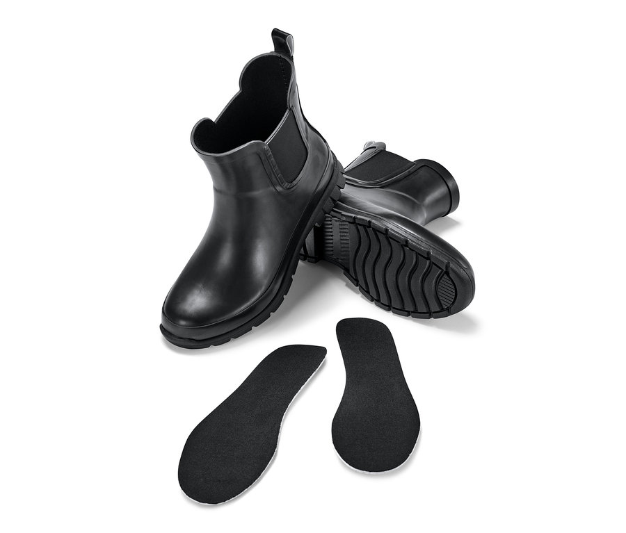 Deux paires de Chelsea boots imperméables noires pour enfant et deux semelles intérieures noires sur fond blanc.