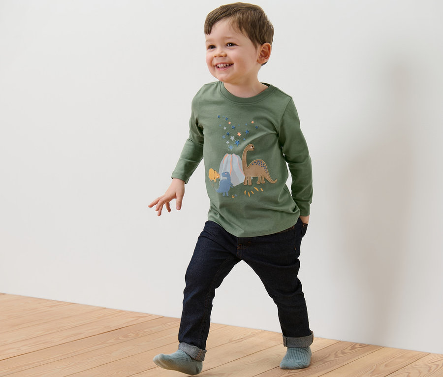 Un garçon marche sur un plancher en bois et porte un 2	-shirts manches longues pour enfant, dinosaure.