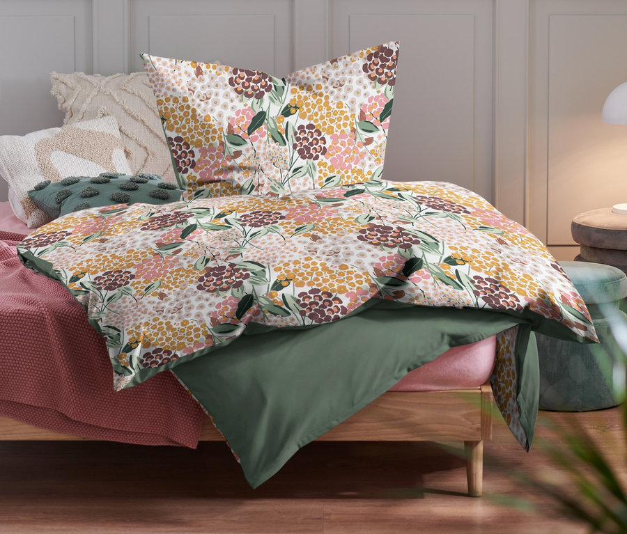 Sur un lit, trois parures de lit en renforcé de taille normale et une parure de lit en renforcé de grande taille avec un motif floral.