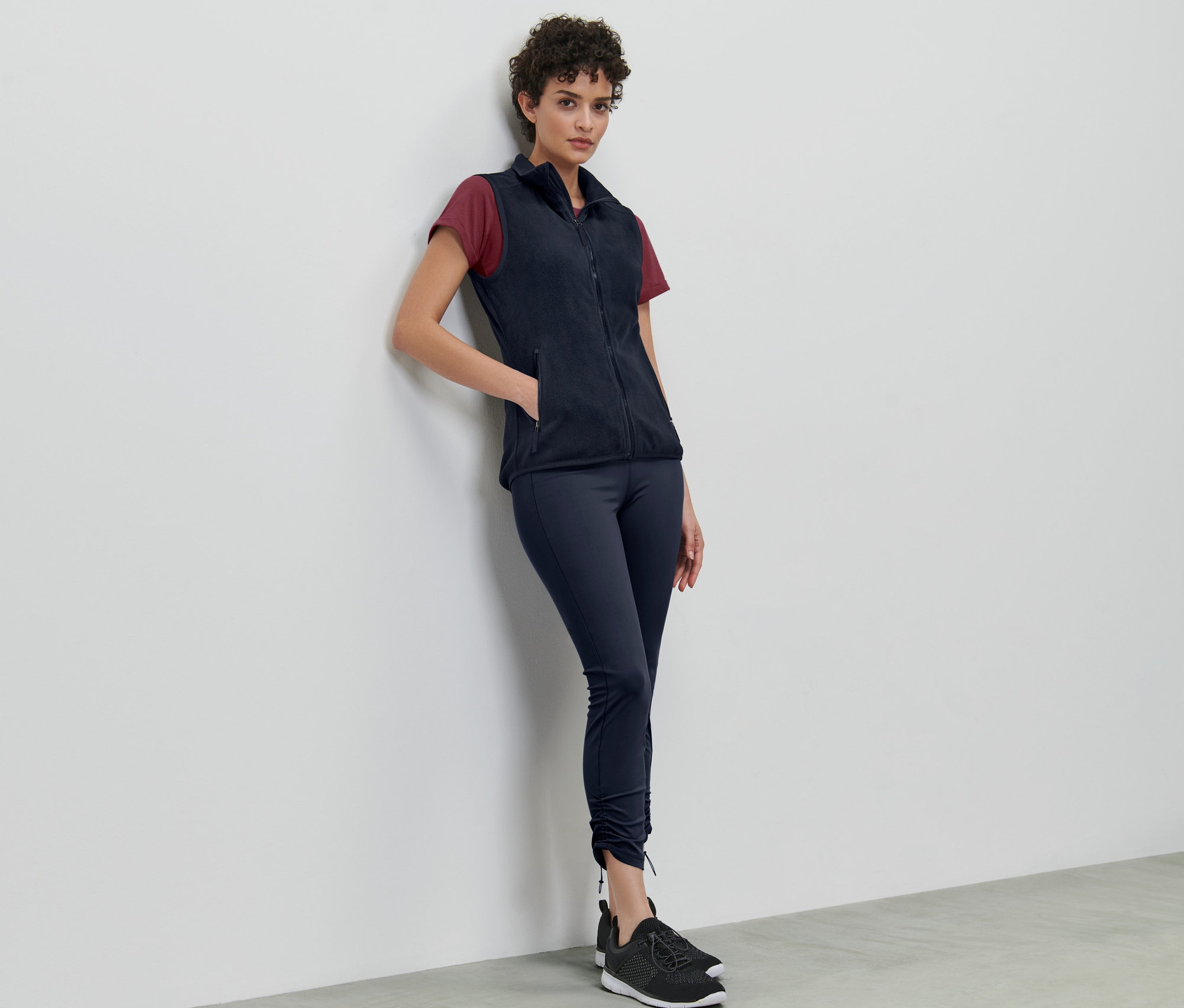 Une femme appuyée contre un mur porte un gilet sans manches en polaire.