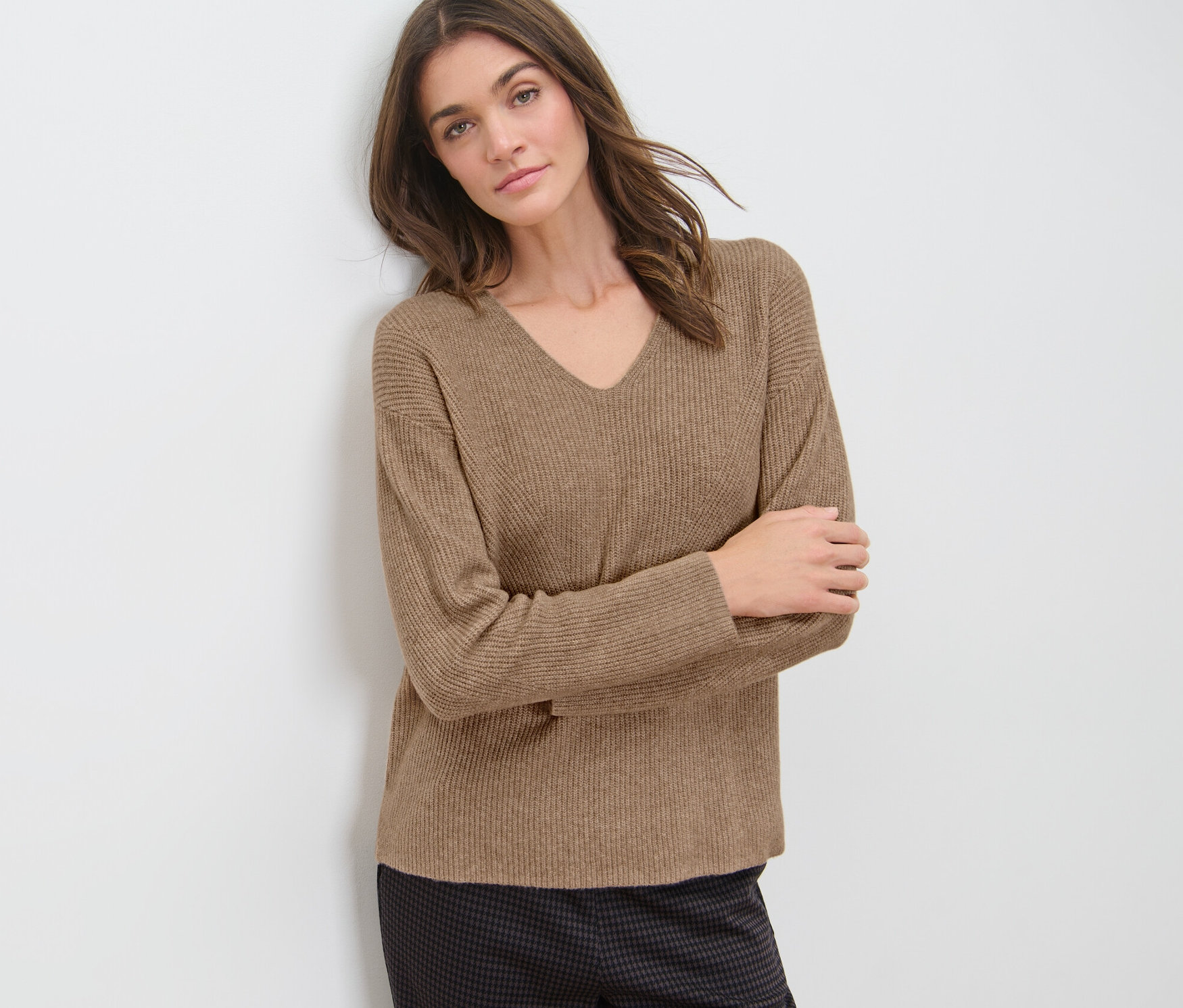 Femme appuyée contre un mur portant un pull camel en grosse maille.