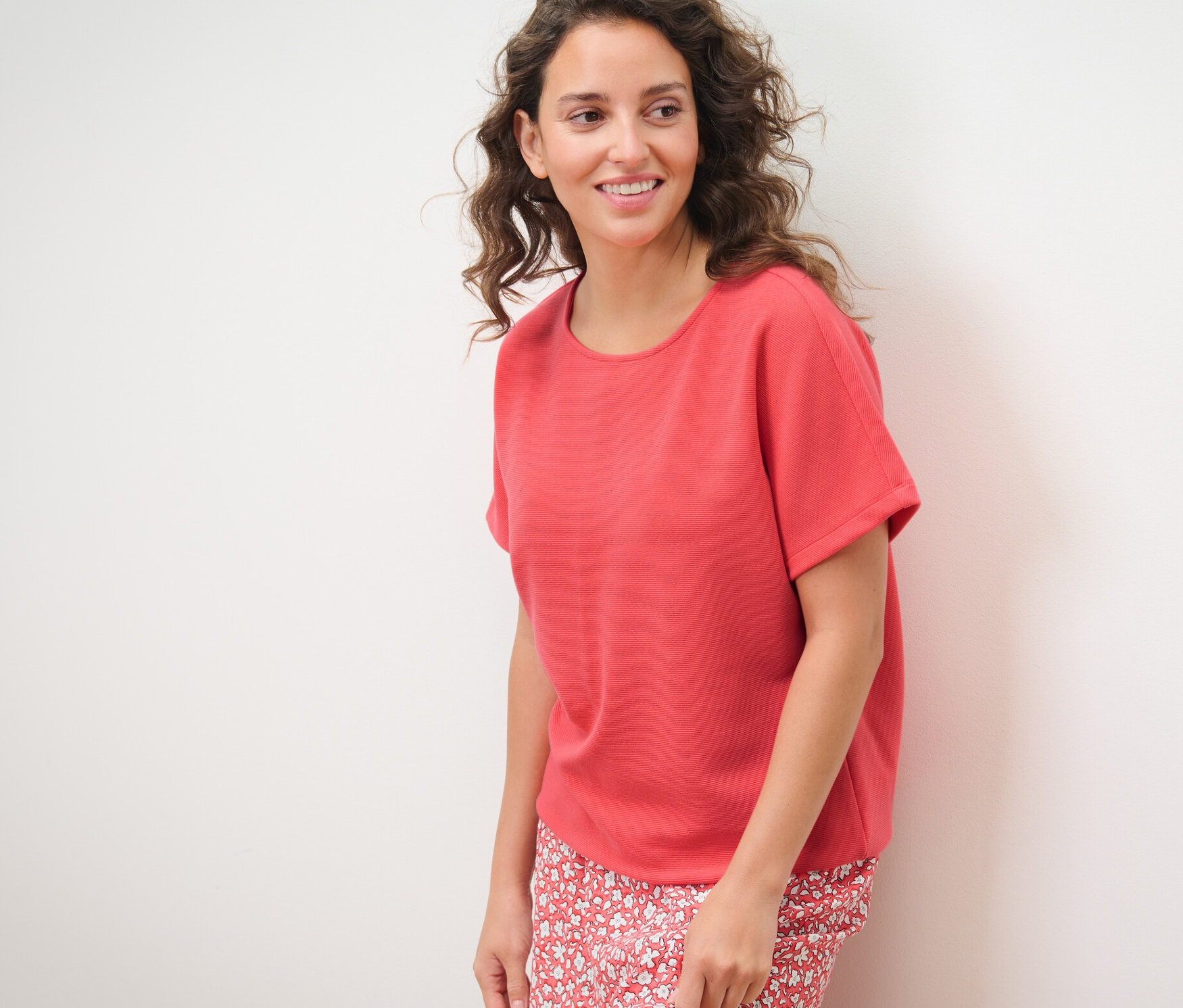 Une femme pose sur un fond blanc et porte un chemisier corail.