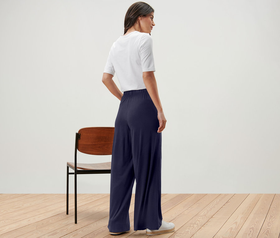 Une femme, vue de dos, porte un pantalon palazzo bleu foncé et un t-shirt blanc.
