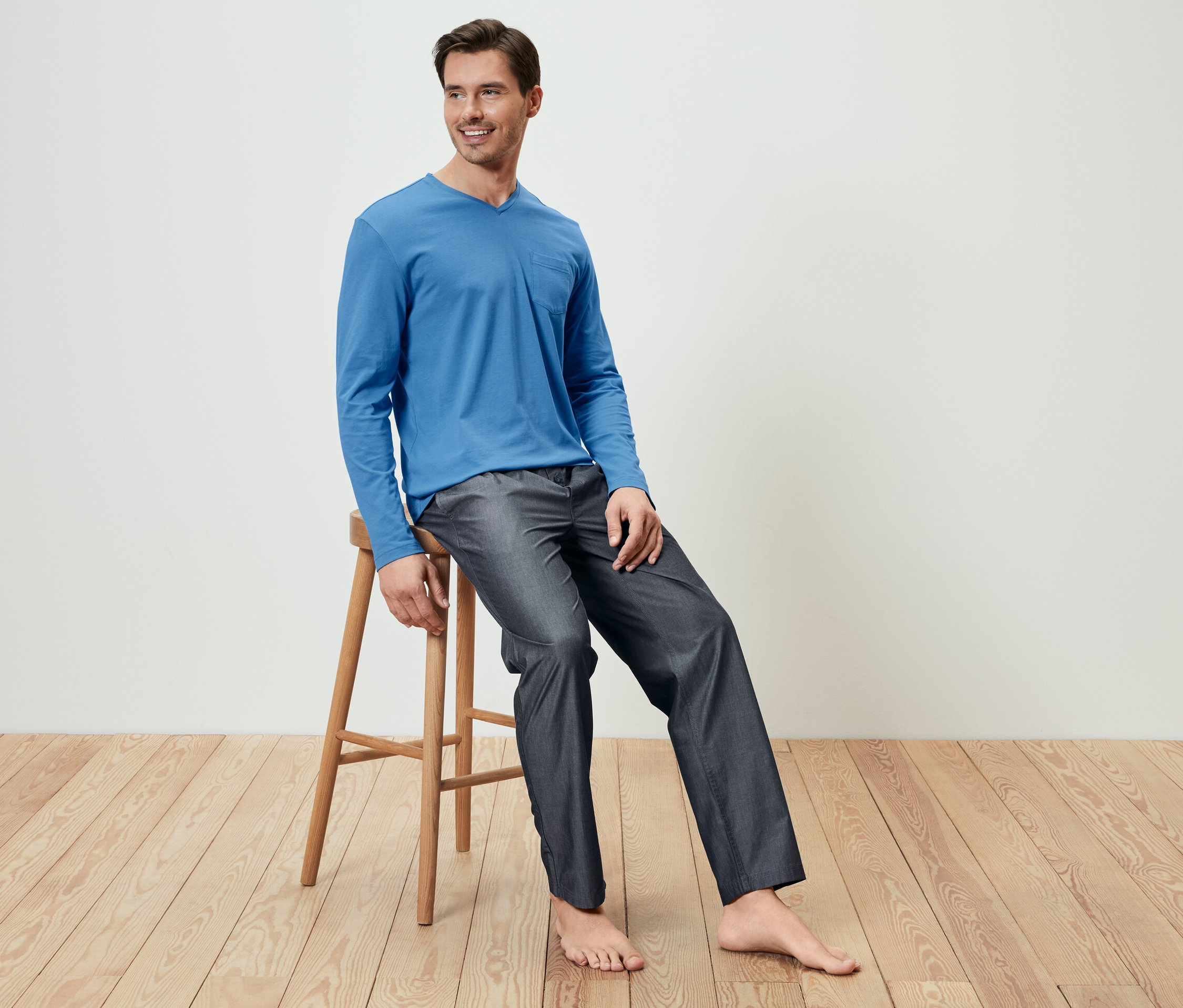 Un homme est assis sur un tabouret en bois et porte un haut de pyjama bleu et un pantalon tissé.