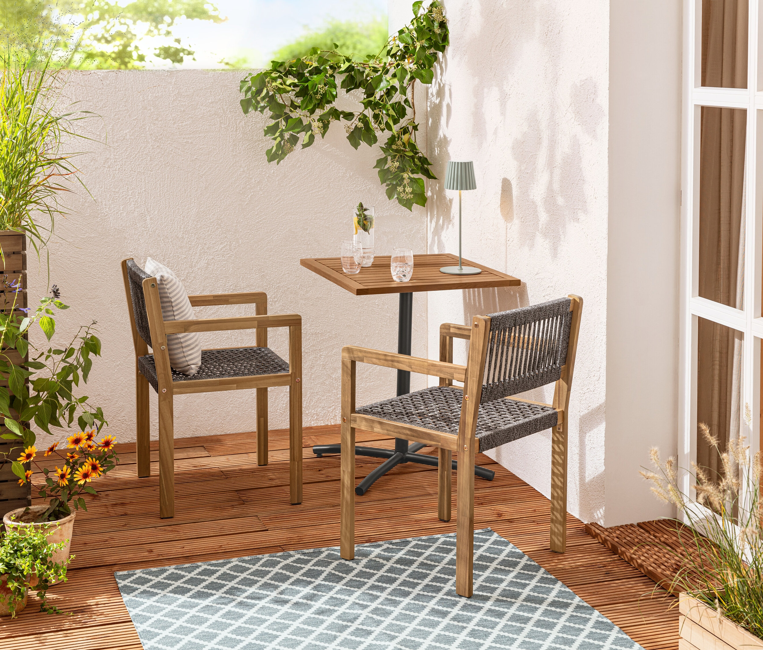 Deux chaises de salle à manger en osier sont placées près d'une table de balcon «
Elin
» sur un tapis d’extérieur réversible.