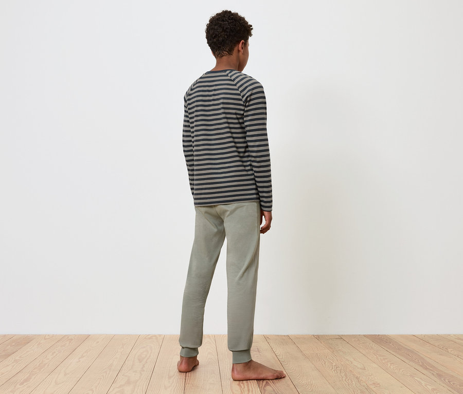 Un garçon se tient dos à la caméra, portant un haut à manches longues rayé gris et un pantalon de survêtement gris.