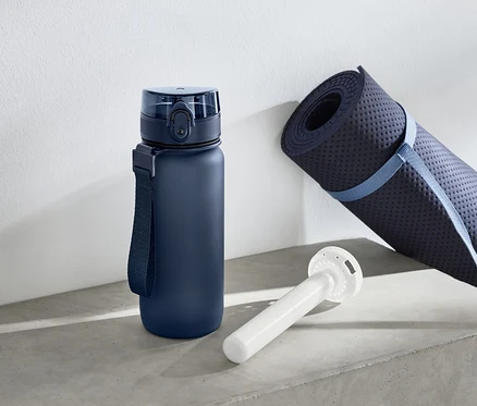 Une bouteille d'eau bleue est à côté d'un tapis de yoga enroulé et d'un objet cylindrique blanc.
