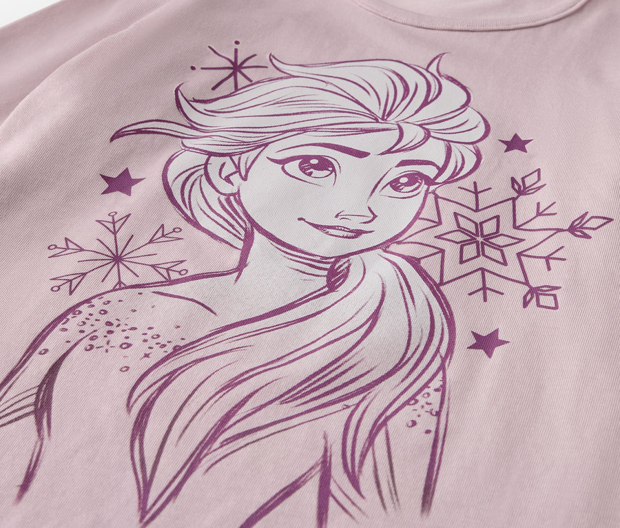 Gros plan sur un ensemble pyjama pour enfant « Princesse des glaces » avec un dessin d'Elsa, des flocons de neige et des étoiles sur un t-shirt rose.
