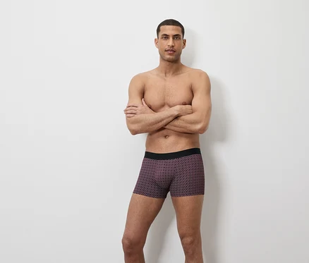 Un homme pose, les bras croisés, portant un boxer à motifs géométriques.